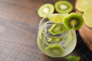 Photo of Glass of refreshing drink with kiwi and lime on wooden table, closeup. Space for text