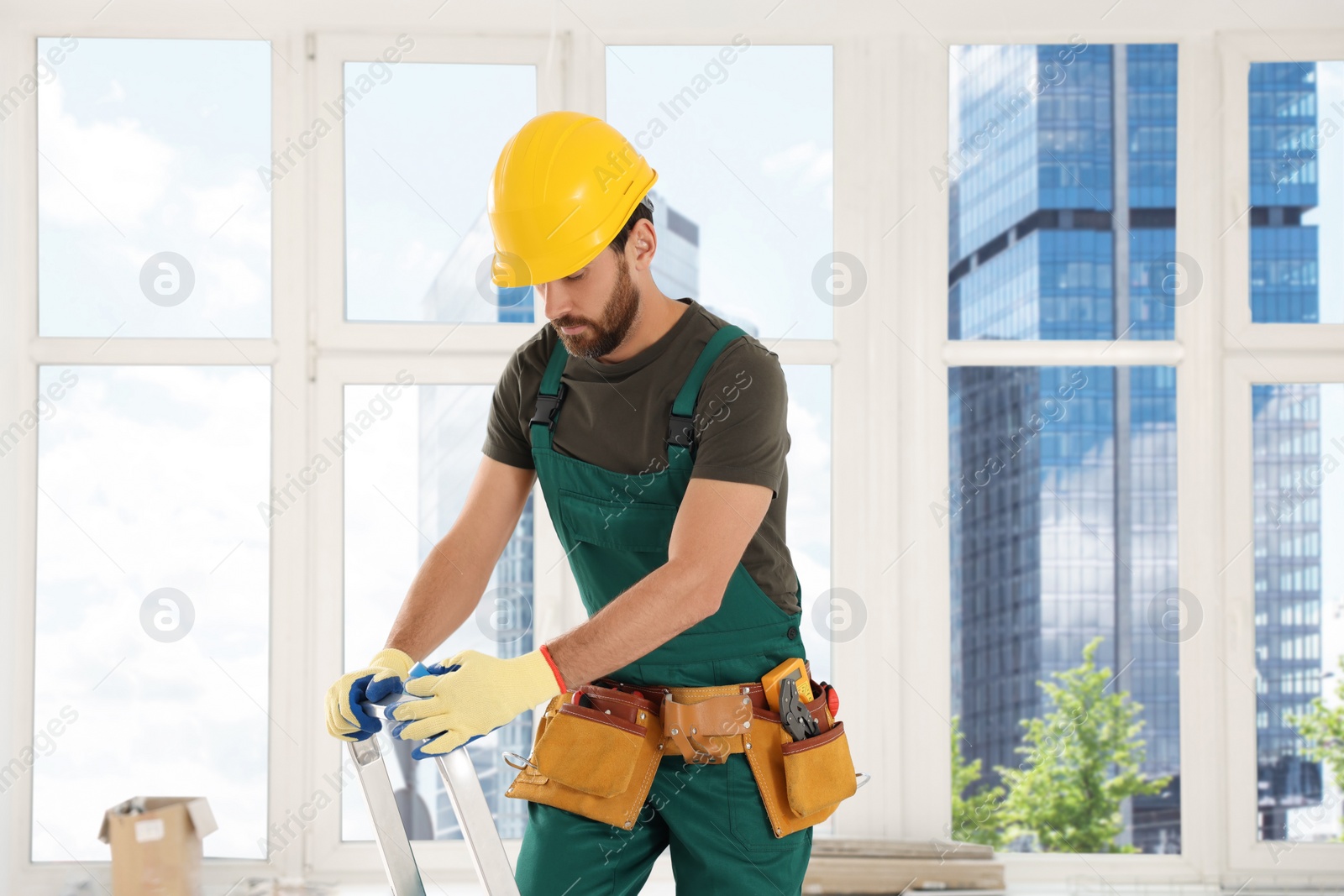 Photo of Professional electrician standing on metal ladder indoors