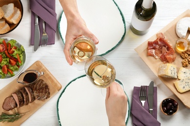 Photo of Man and woman holding glasses of white wine over table with delicious food, top view