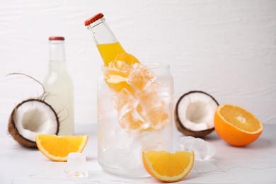 Tasty kombucha in bottles, glass with ice and fresh fruits on white table