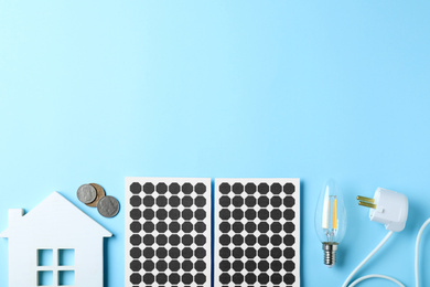 Photo of Flat lay composition with solar panels, house model, light bulb and and coins on light blue background. Space for text