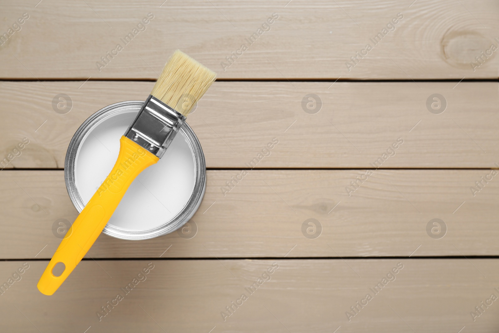 Photo of Can of white paint with brush on wooden table, top view. Space for text