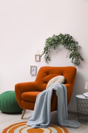 Stylish room decorated with beautiful eucalyptus garland above comfortable orange armchair