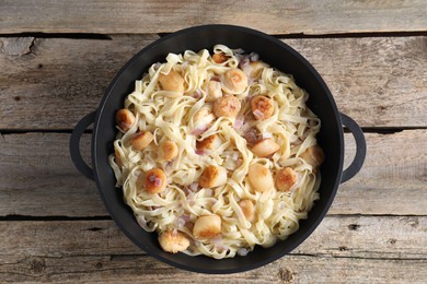 Photo of Delicious scallop pasta with onion in pan on wooden table, top view