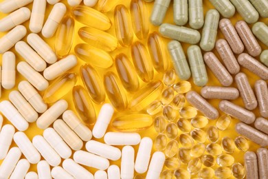 Many different vitamin capsules on yellow background, flat lay