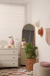 Photo of Chest of drawers, mirror and houseplant in bedroom. Stylish interior