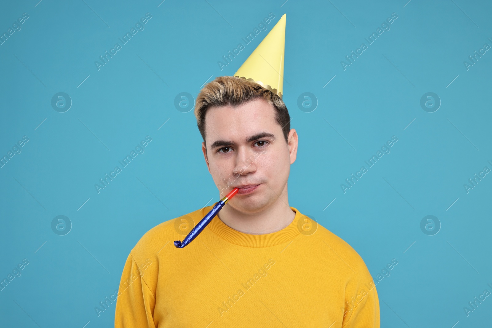 Photo of Young man with party hat and blower on light blue background