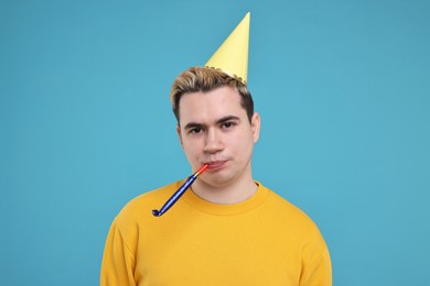 Photo of Young man with party hat and blower on light blue background