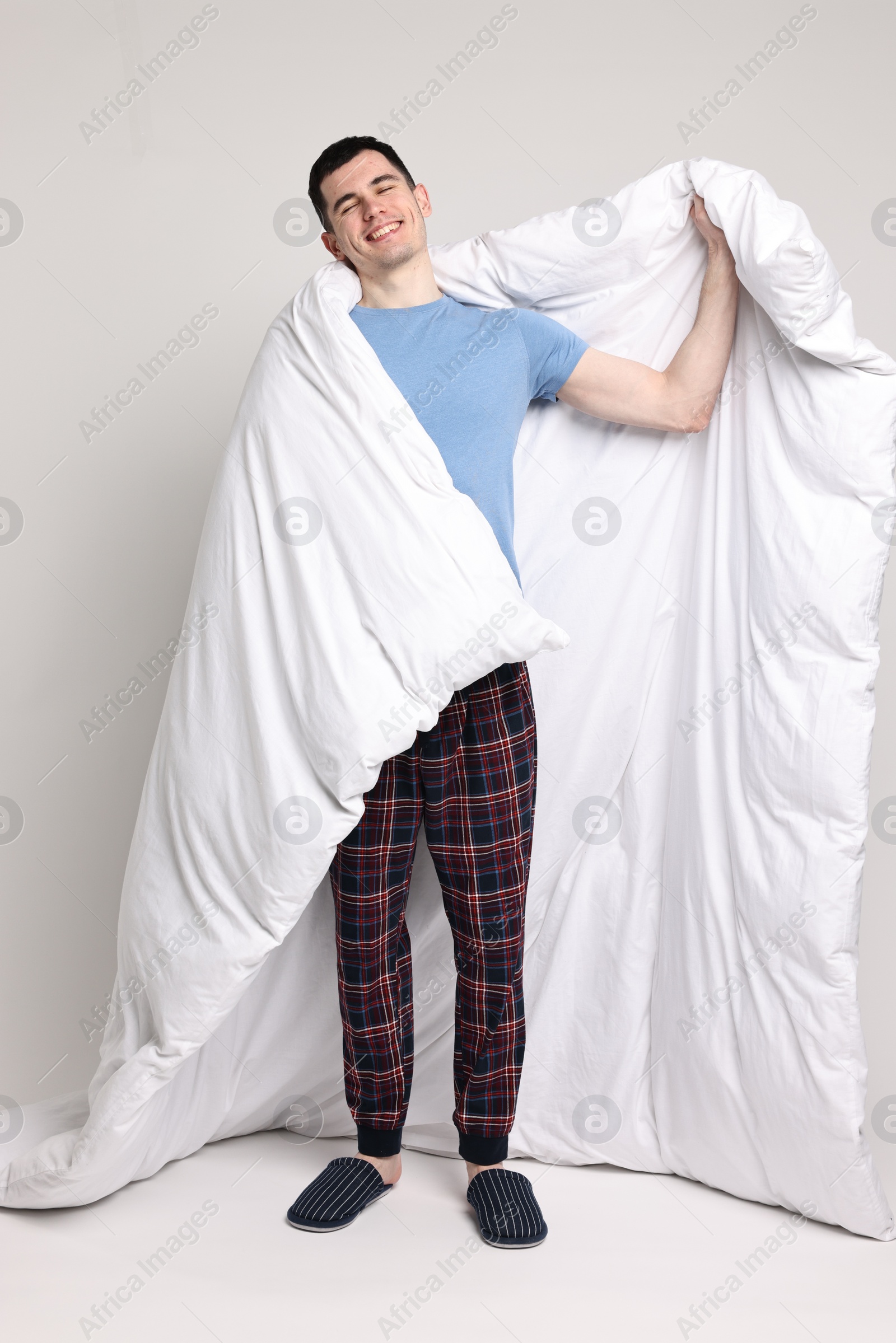 Photo of Happy man in pyjama wrapped in blanket on light grey background