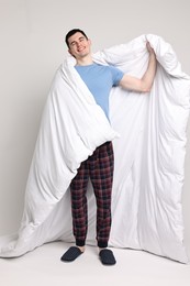 Photo of Happy man in pyjama wrapped in blanket on light grey background