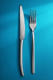 Photo of Shiny fork and knife on light blue background, flat lay