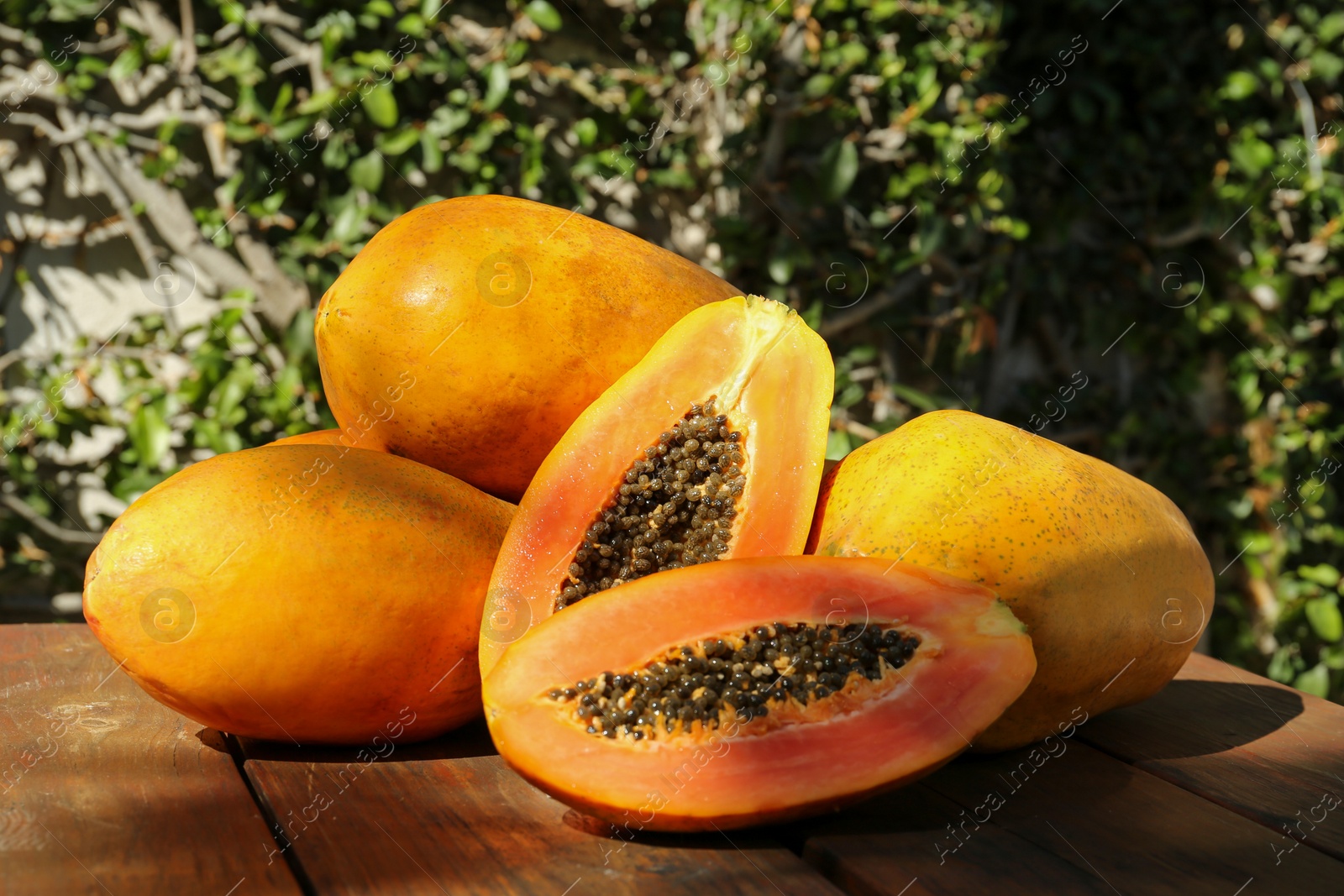 Photo of Fresh ripe cut and whole papaya fruits on wooden table outdoors