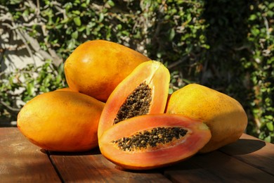 Fresh ripe cut and whole papaya fruits on wooden table outdoors