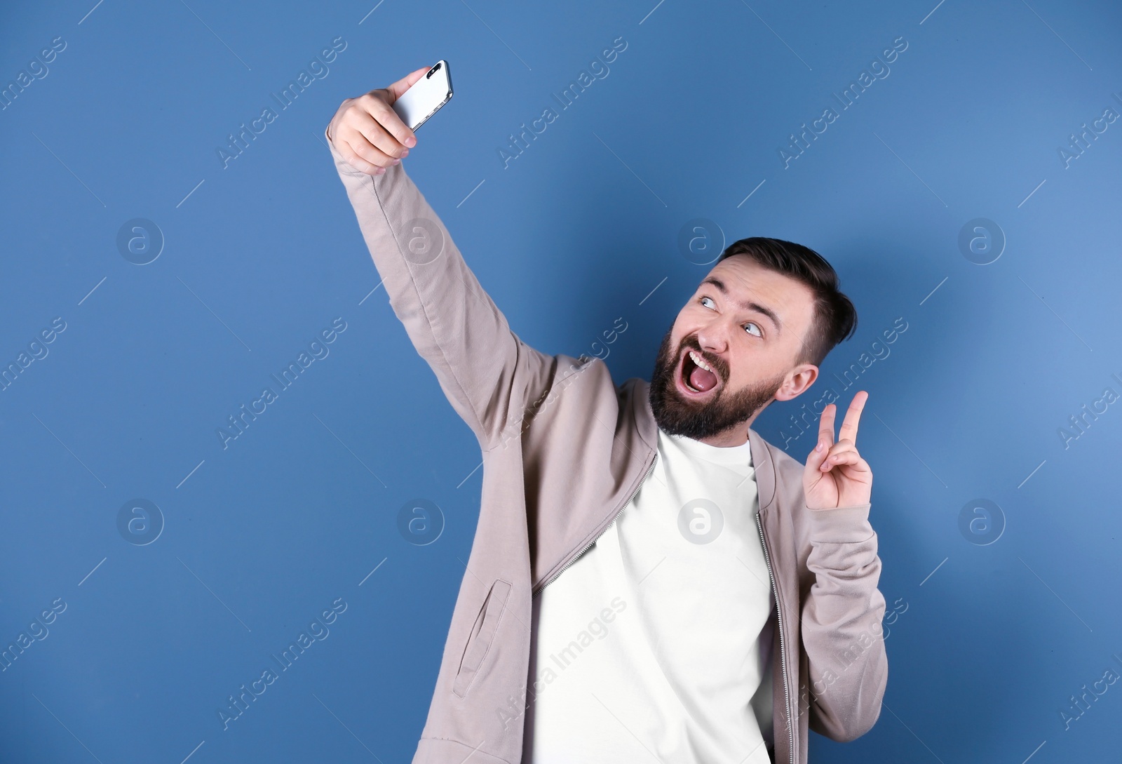 Photo of Handsome bearded man taking selfie on color background