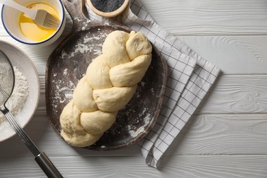 Photo of Homemade braided bread and ingredients on white wooden table, flat lay. Cooking traditional Shabbat challah