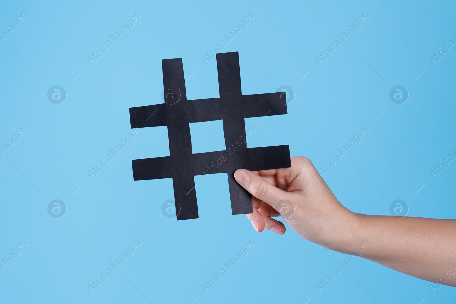 Photo of Woman holding black paper cutout symbol of hashtag on turquoise background, closeup