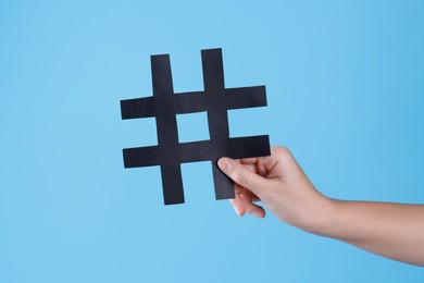 Photo of Woman holding black paper cutout symbol of hashtag on turquoise background, closeup
