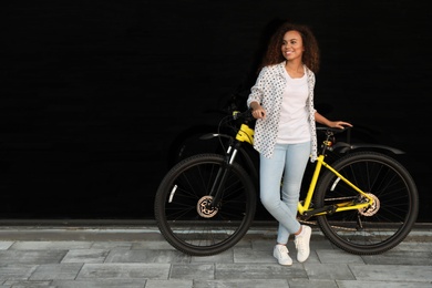 Photo of Beautiful young African-American woman with bicycle near glass building. Space for text