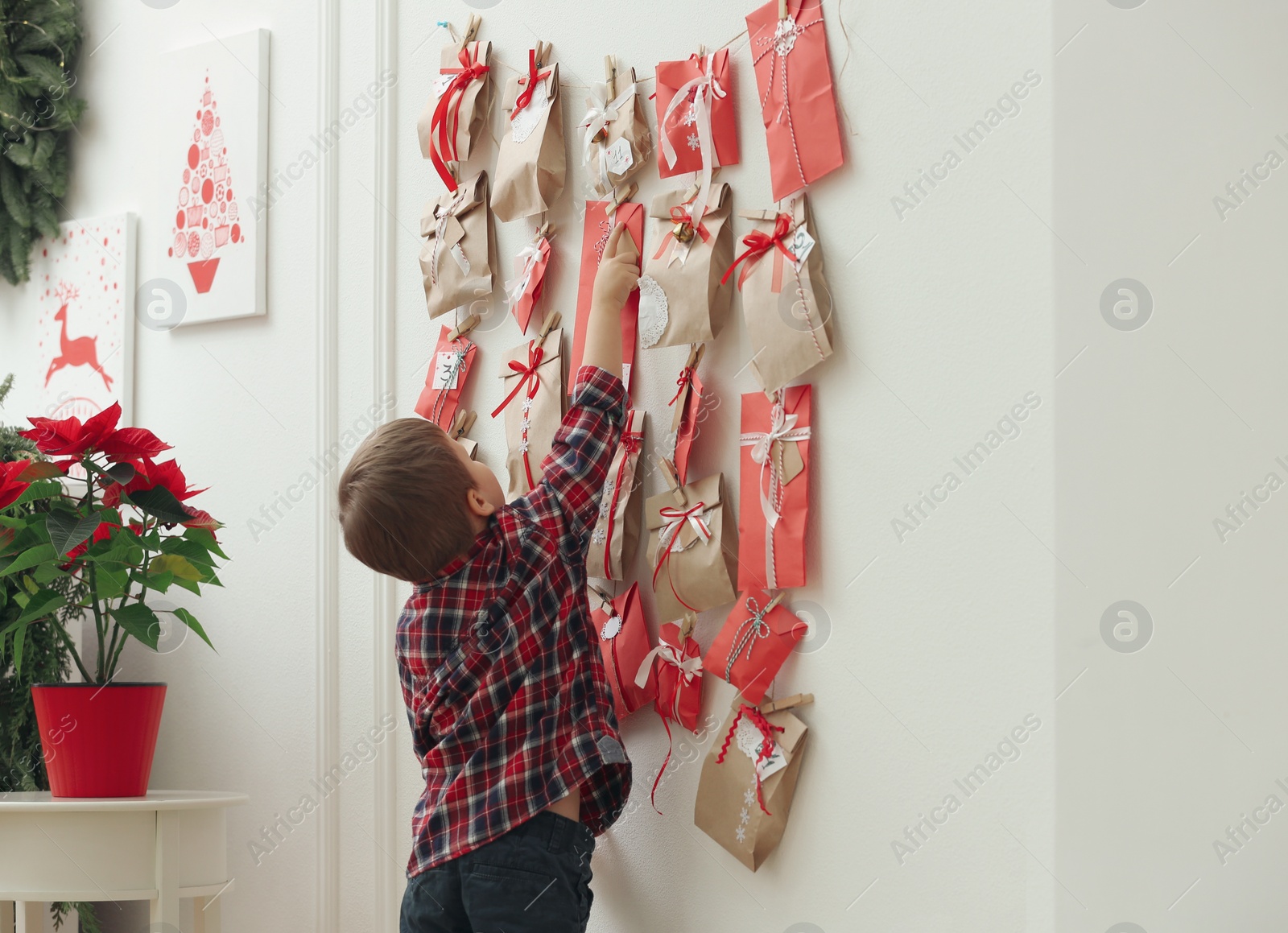 Photo of Cute little boy taking gift from Advent calendar at home. Christmas tradition