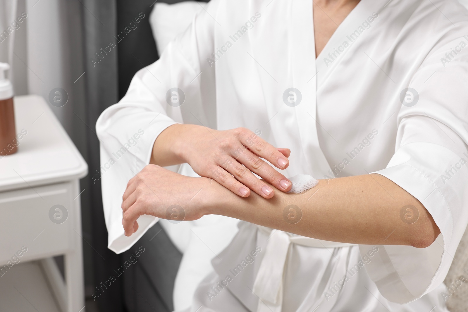 Photo of Woman applying self-tanning product onto arm indoors, closeup