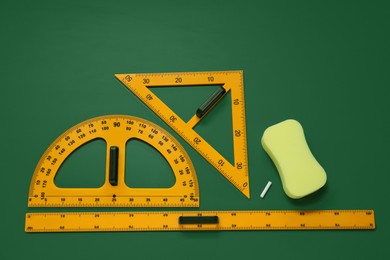 Photo of Protractor, triangle, ruler and sponge on green chalkboard, flat lay