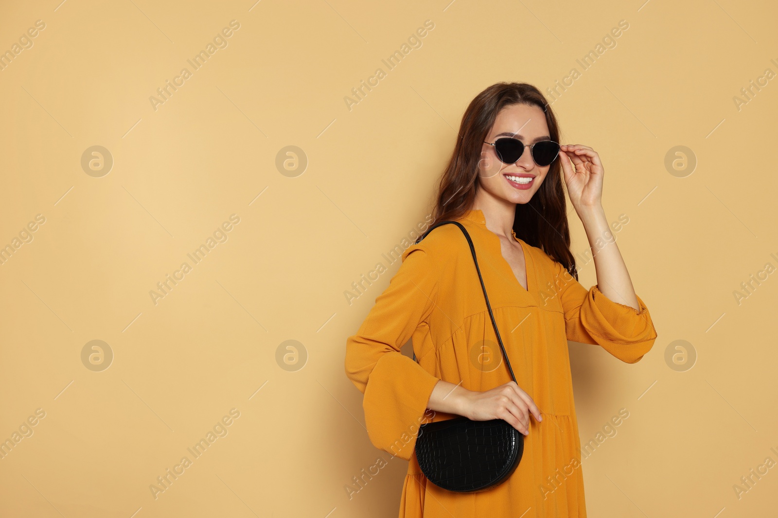 Photo of Beautiful young woman in fashionable outfit with stylish bag on beige background, space for text