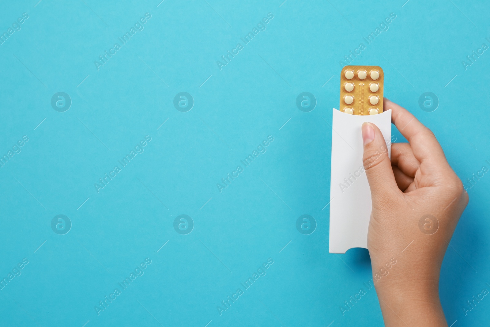 Photo of Woman holding blister with birth control pills on light blue background, top view. Space for text