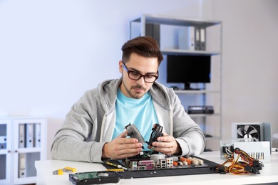 Male technician repairing motherboard at table indoors