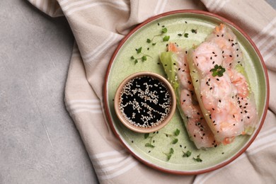 Photo of Plate with tasty spring rolls served with soy sauce on grey textured table, top view. Space for text