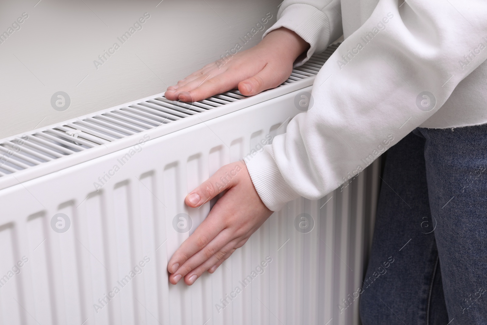 Photo of Girl warming hands on heating radiator indoors, closeup