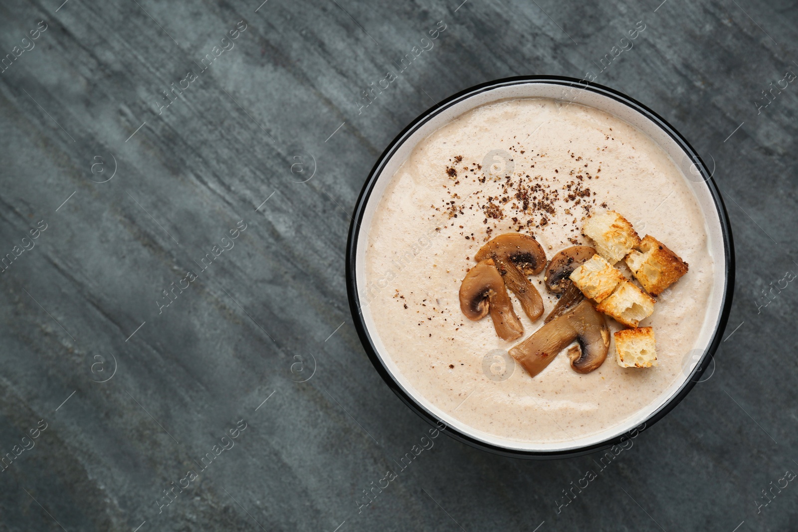 Photo of Delicious cream soup with mushrooms and croutons on black table, top view. Space for text