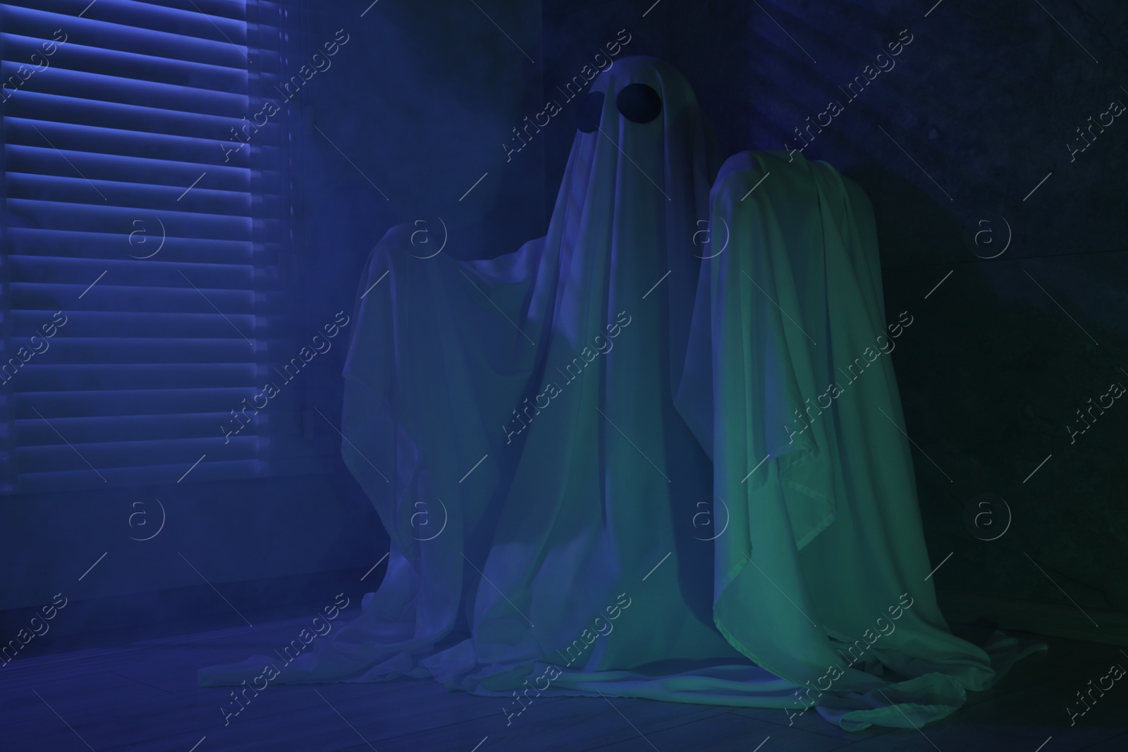 Photo of Creepy ghost. Woman covered with sheet near window in blue light