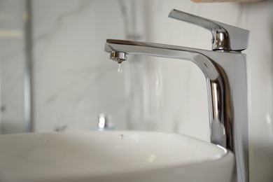 Photo of Water drop falling down from tap on blurred background, closeup