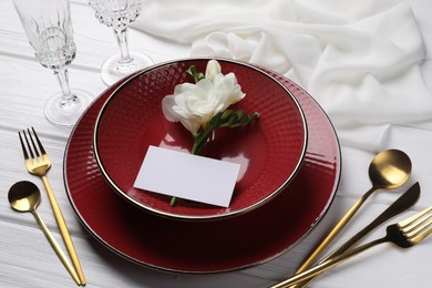 Stylish table setting. Dishes, cutlery, blank card and flower on white wooden background