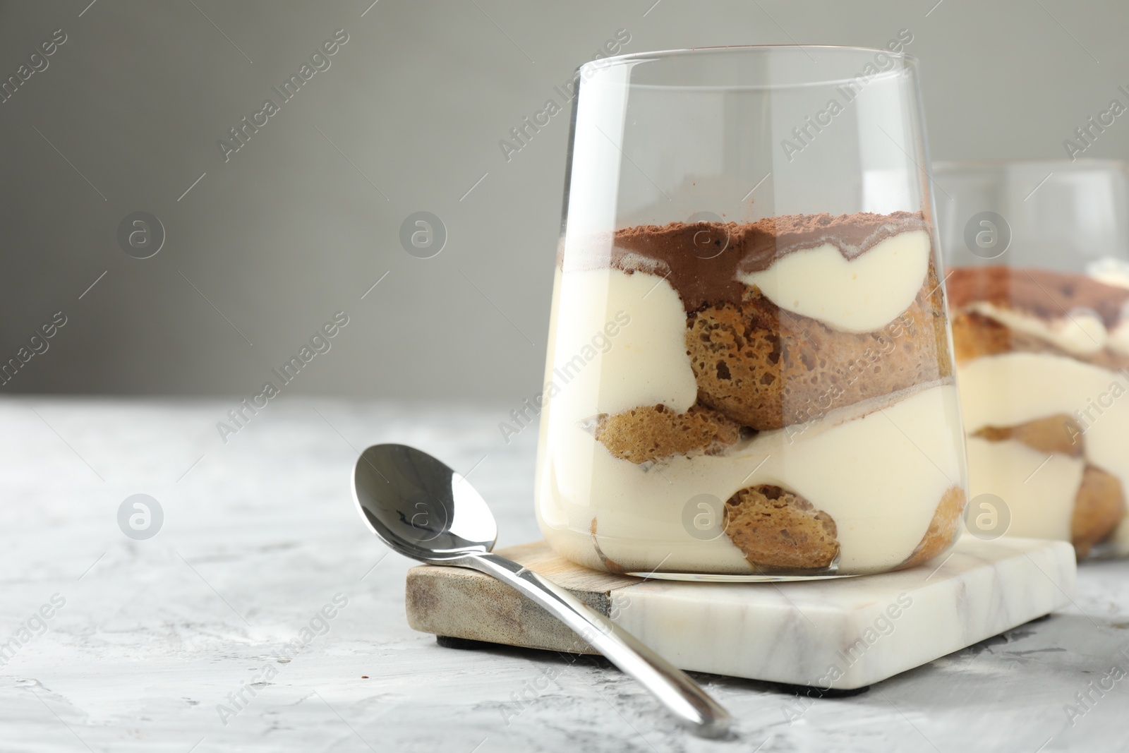 Photo of Delicious tiramisu in glasses and spoon on grey textured table, closeup. Space for text