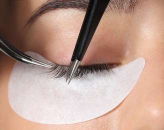 Photo of Young woman undergoing eyelashes extensions procedure, closeup