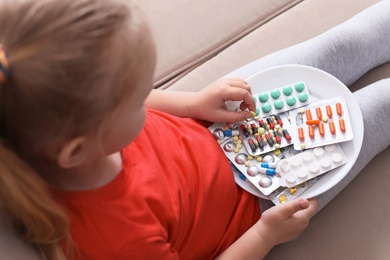Photo of Little child with plate of different pills at home. Household danger