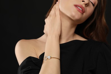 Photo of Young woman wearing elegant pearl bracelet on black background, closeup