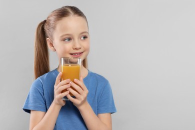 Cute little girl with glass of fresh juice on light gray background, space for text