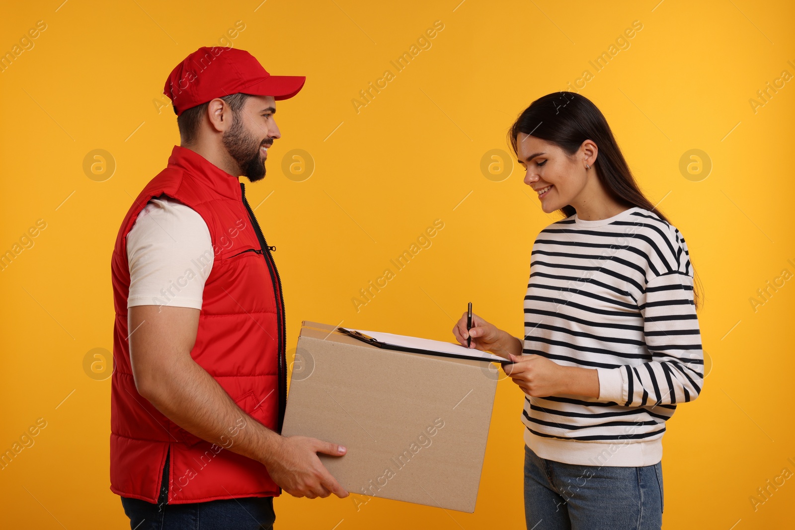 Photo of Happy young woman signing order receipt on orange background. Courier delivery