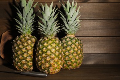 Photo of Whole ripe pineapples and knife on wooden table