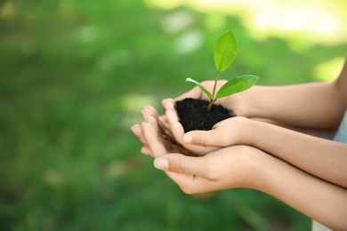 Photo of Woman and her child holding soil with green plant in hands on blurred background. Family concept