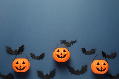 Photo of Flat lay composition with plastic pumpkin baskets and paper bats on dark blue background, space for text. Halloween celebration