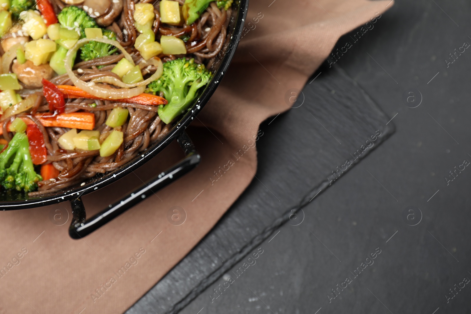 Photo of Stir fried noodles with mushrooms and vegetables in wok on black table, top view. Space for text