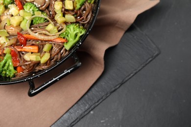 Stir fried noodles with mushrooms and vegetables in wok on black table, top view. Space for text