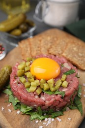 Tasty beef steak tartare served with yolk, pickled cucumber and other accompaniments on wooden board, closeup