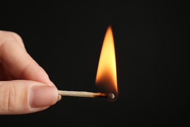 Photo of Woman holding burning match on black background, closeup. Space for text