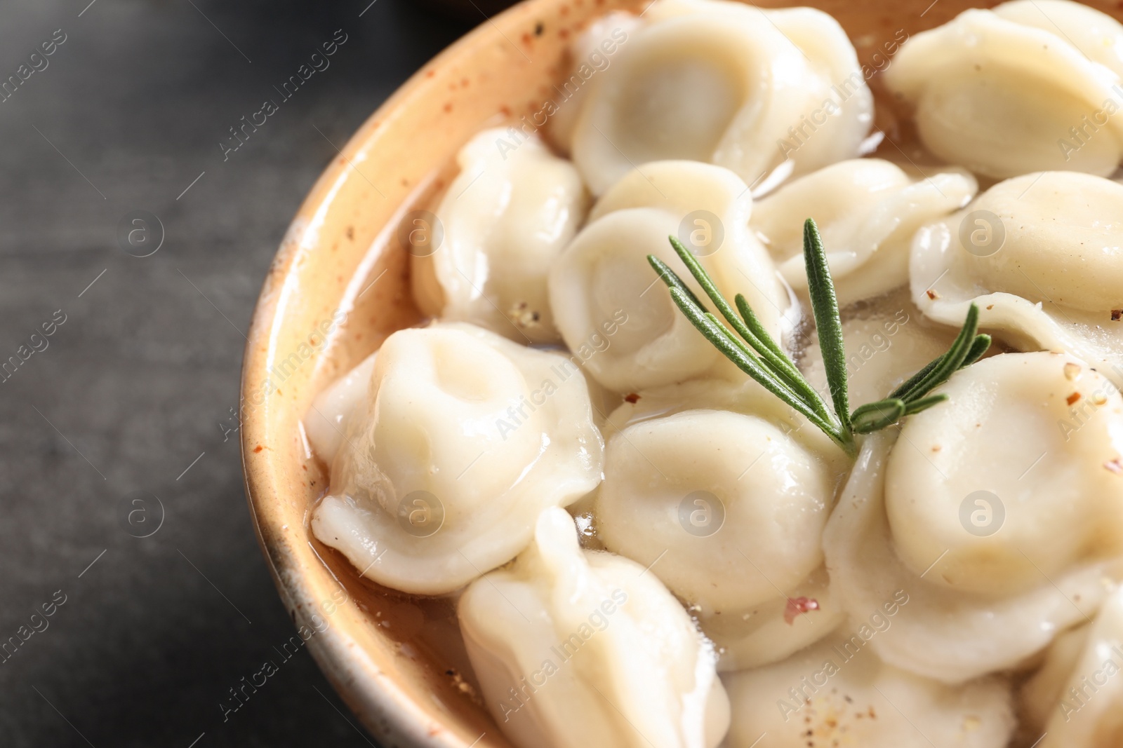 Photo of Bowl of tasty dumplings in broth on table, closeup