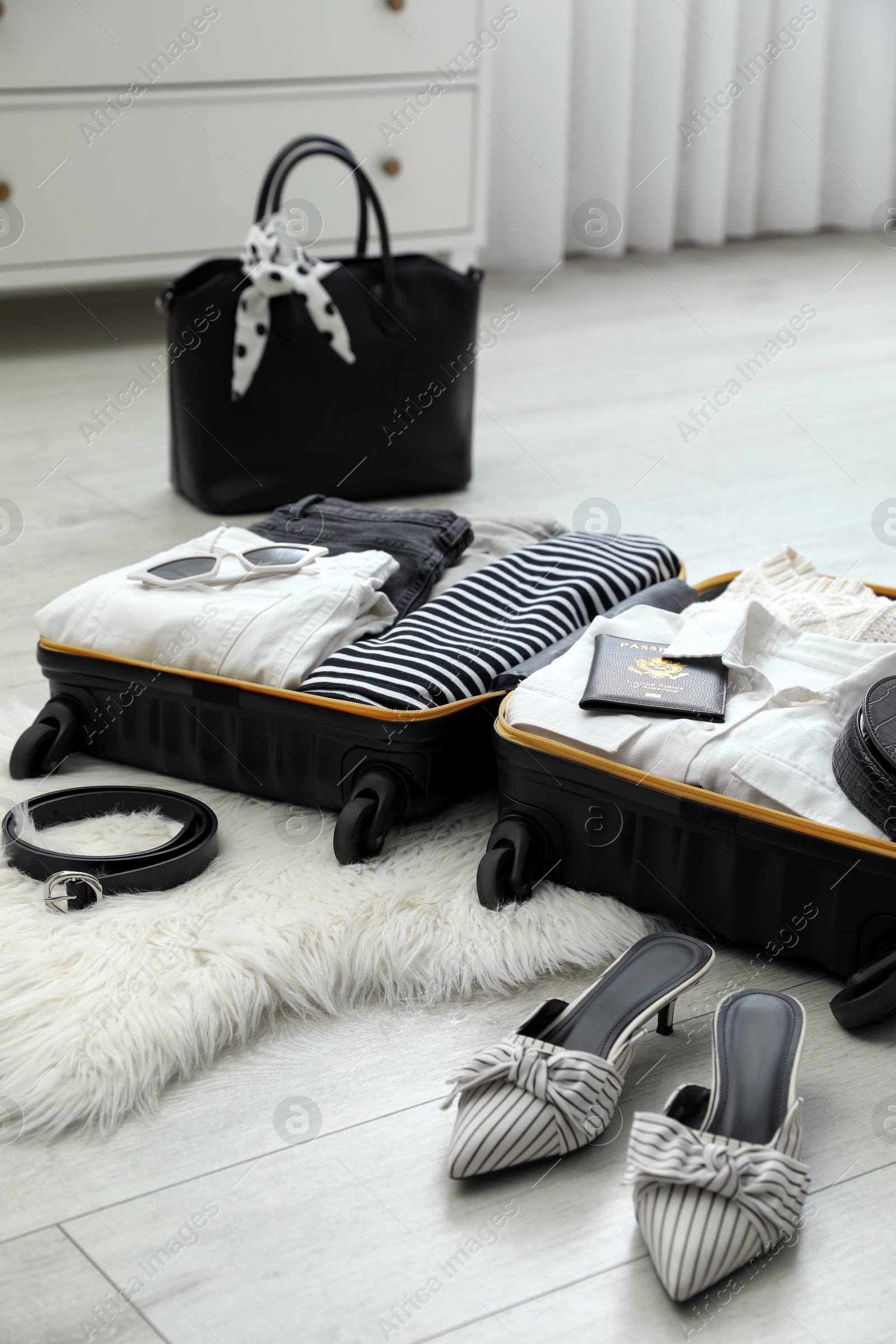 Photo of Open suitcase with clothes, shoes and accessories on floor indoors