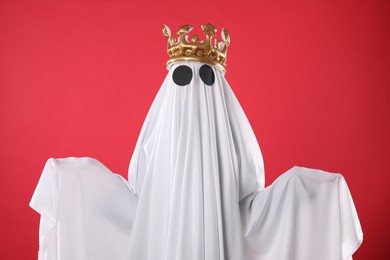 Person in ghost costume and luxurious crown on red background